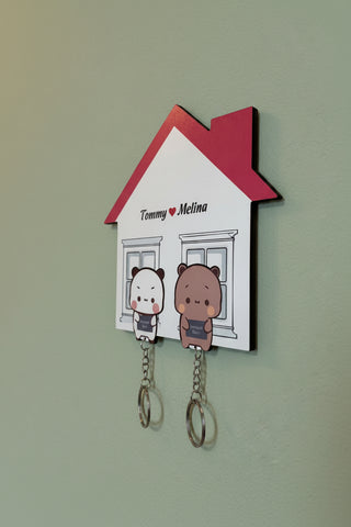 Wall hook shaped like a house with cartoon characters and personalized names on a beige wall.